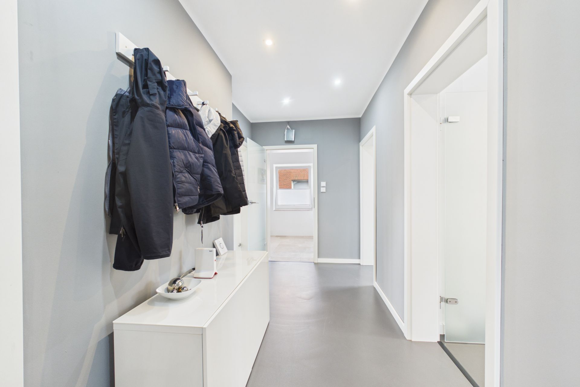 Heller Flur mit grauen Wänden, Kleiderhaken und weißem Schuhschrank.