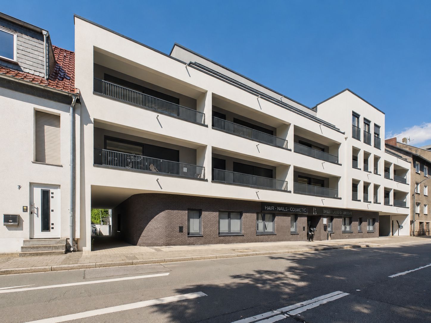 Modernes Wohngebäude mit Balkonen und drei Etagen an einer Straße.