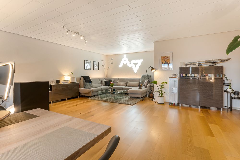 Modernes Wohnzimmer mit Holzfußboden, großem Sofa, Pflanzen und Wanddekoration.