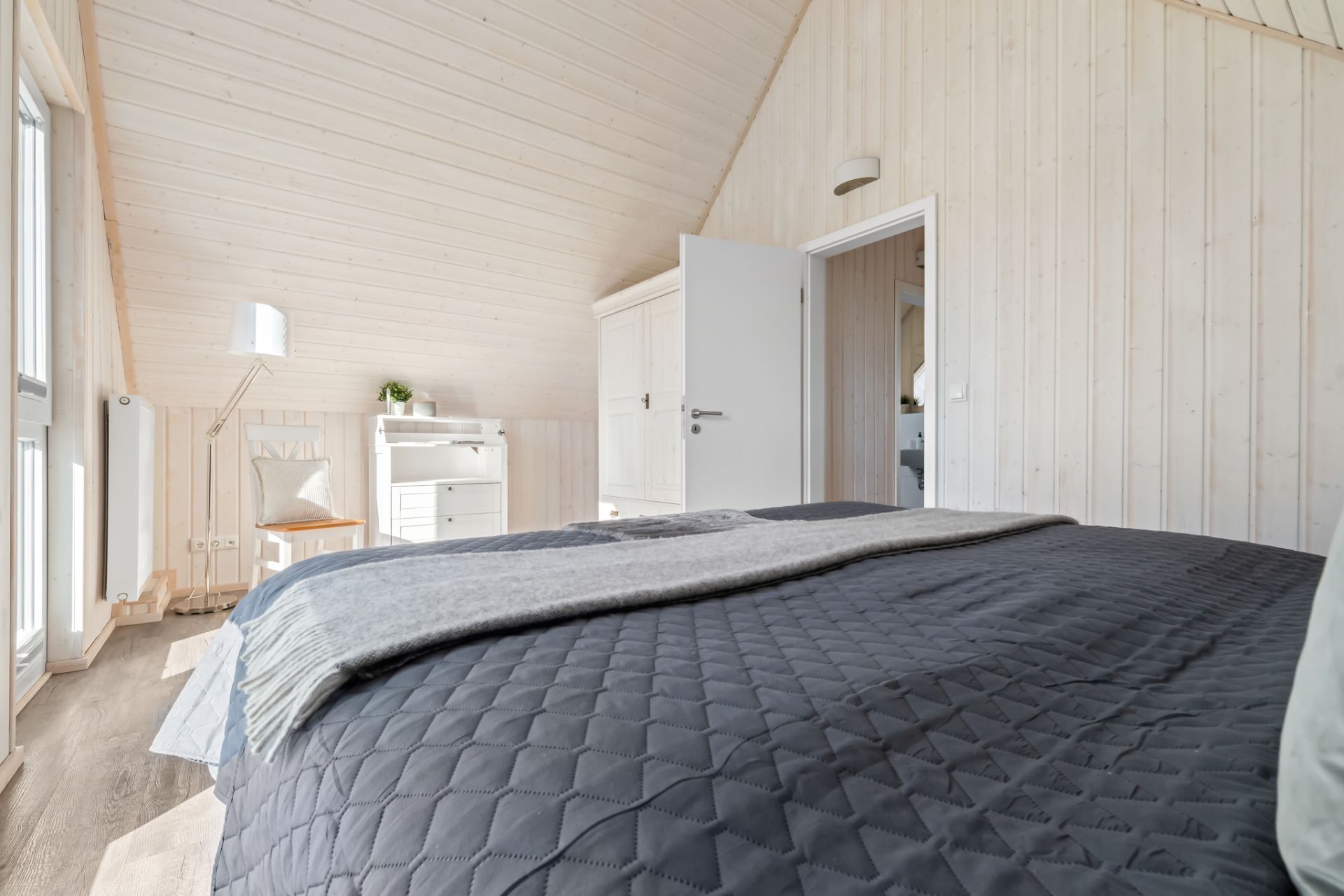 Helles Schlafzimmer mit Bett, Schreibtisch, Stuhl und geöffnetem Kleiderschrank.