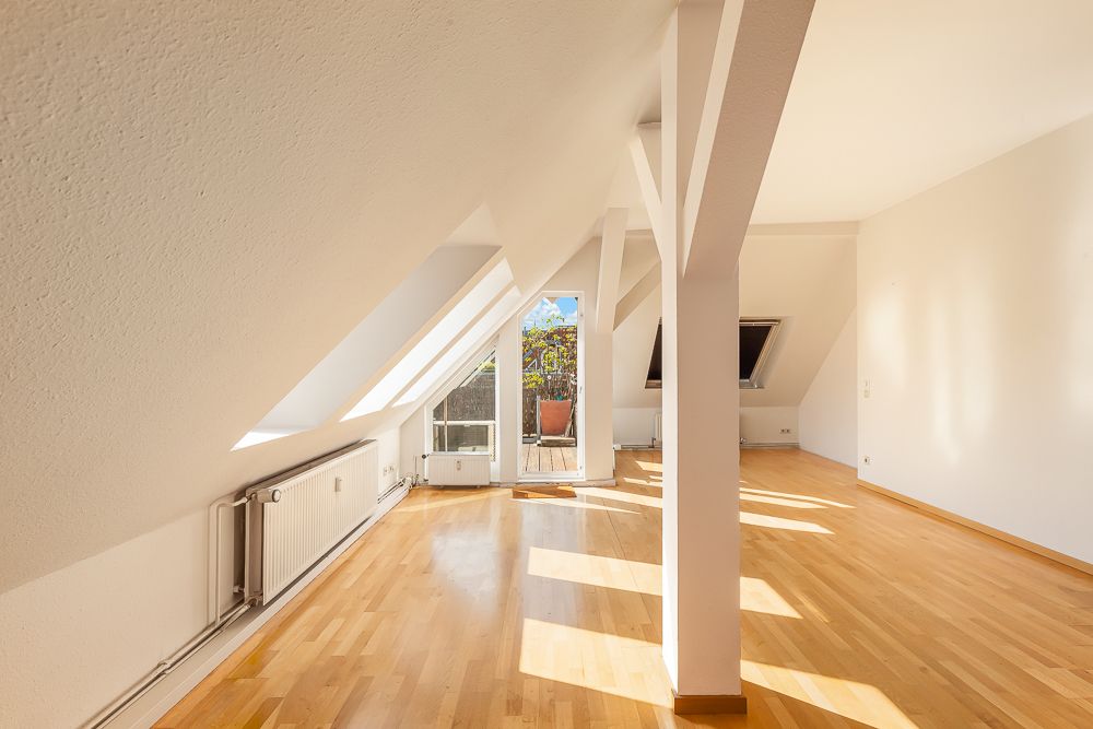 Heller Dachgeschossraum mit Holzboden, Dachschrägen, Fenstern und Zugang zu einem Balkon.