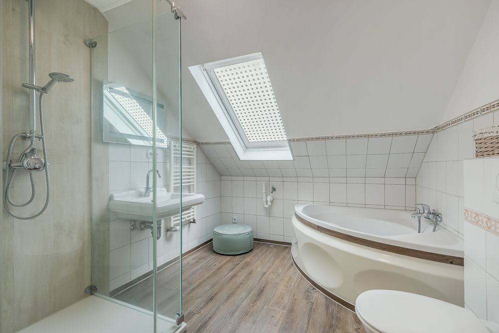 Modernes Badezimmer mit Dusche, Eckbadewanne, Waschbecken und Fenster im Dachgeschoss.