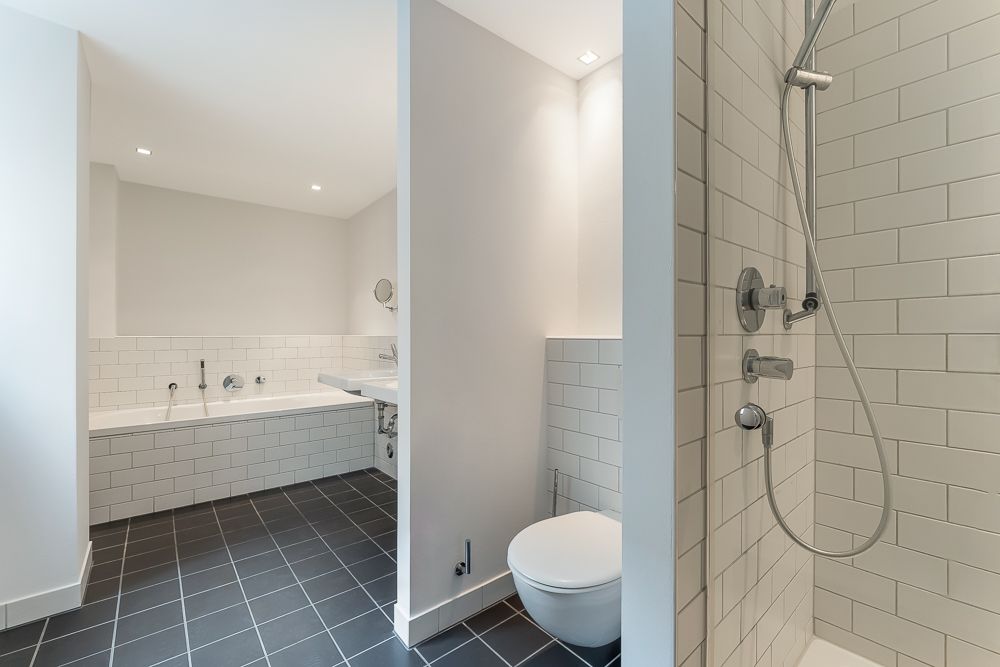 Modernes Badezimmer mit Dusche, Badewanne, WC und Waschbecken. Weiße Fliesen und dunkler Boden.