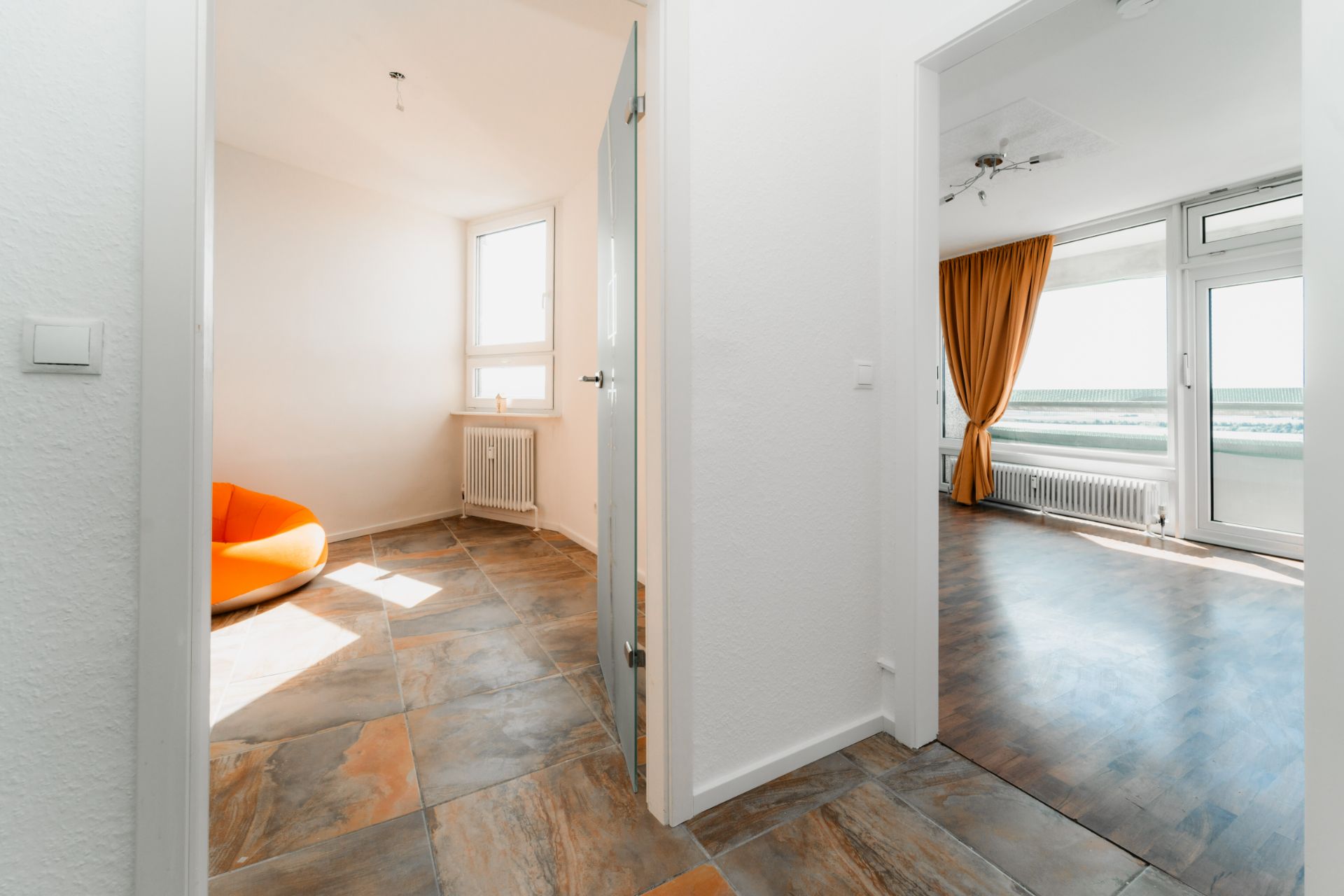 Heller Flur mit Blick in zwei Zimmer, eines mit orangefarbenem Sitzsack, eines mit großen Fenstern und Vorhängen.
