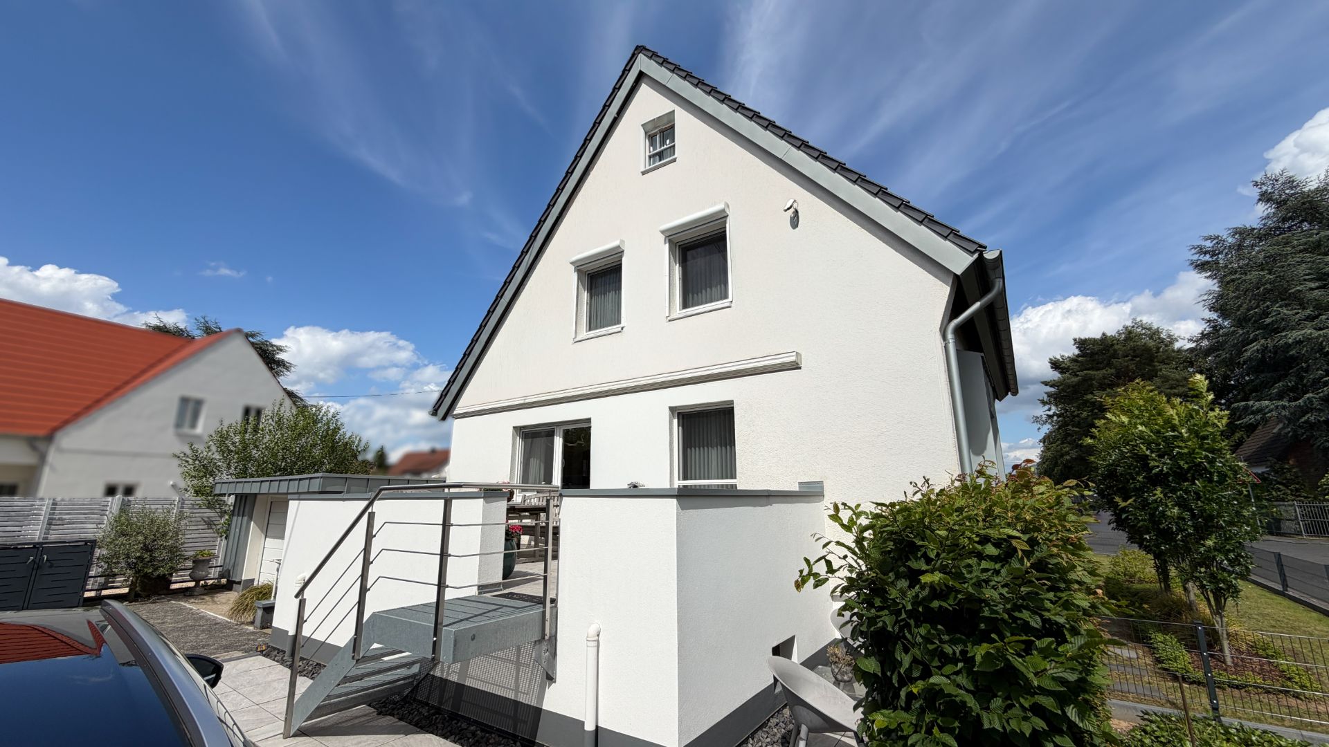 Modernes weißes Einfamilienhaus mit Gartenterrasse und Treppe, umgeben von Bäumen.