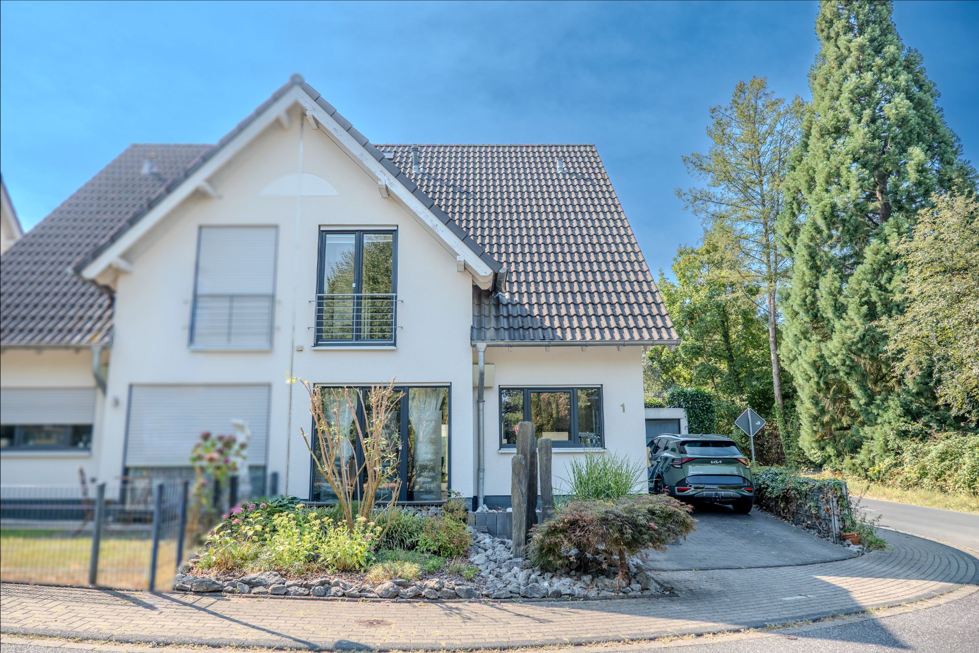 Zweistöckiges Einfamilienhaus mit Garten und Auffahrt, ein Auto steht auf dem Parkplatz.