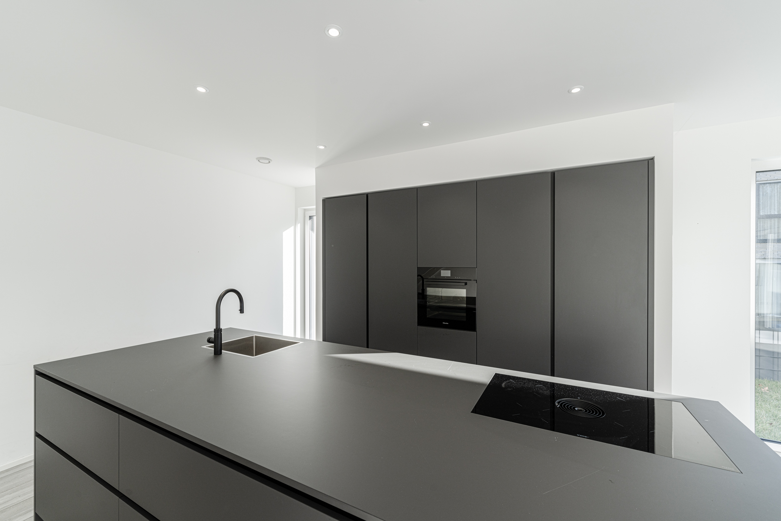 Moderne, minimalistische Küche mit schwarzer Kücheninsel, Herd, Spüle und Einbauschränken.