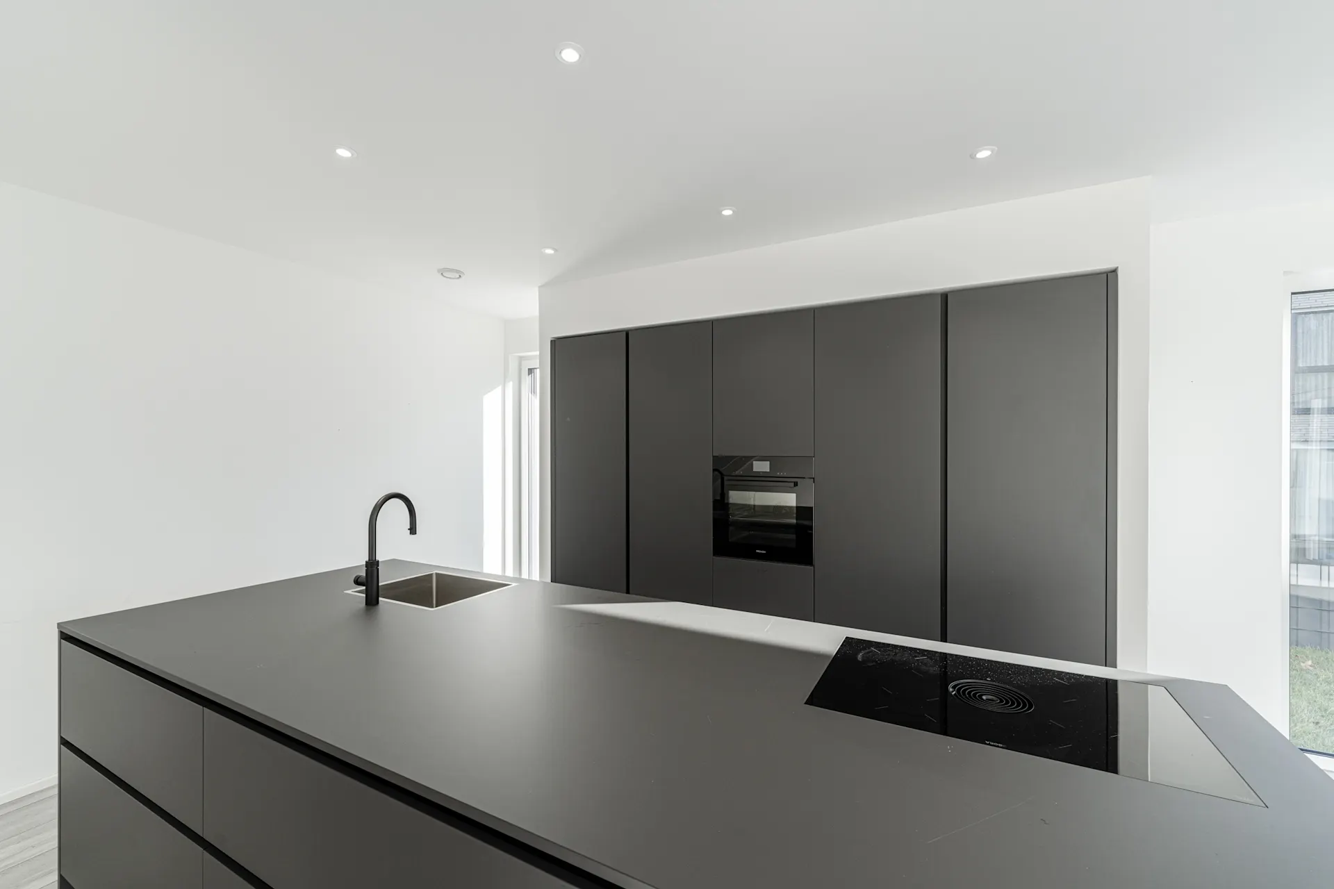 Moderne, minimalistische Küche mit schwarzer Kücheninsel, Herd, Spüle und Einbauschränken.
