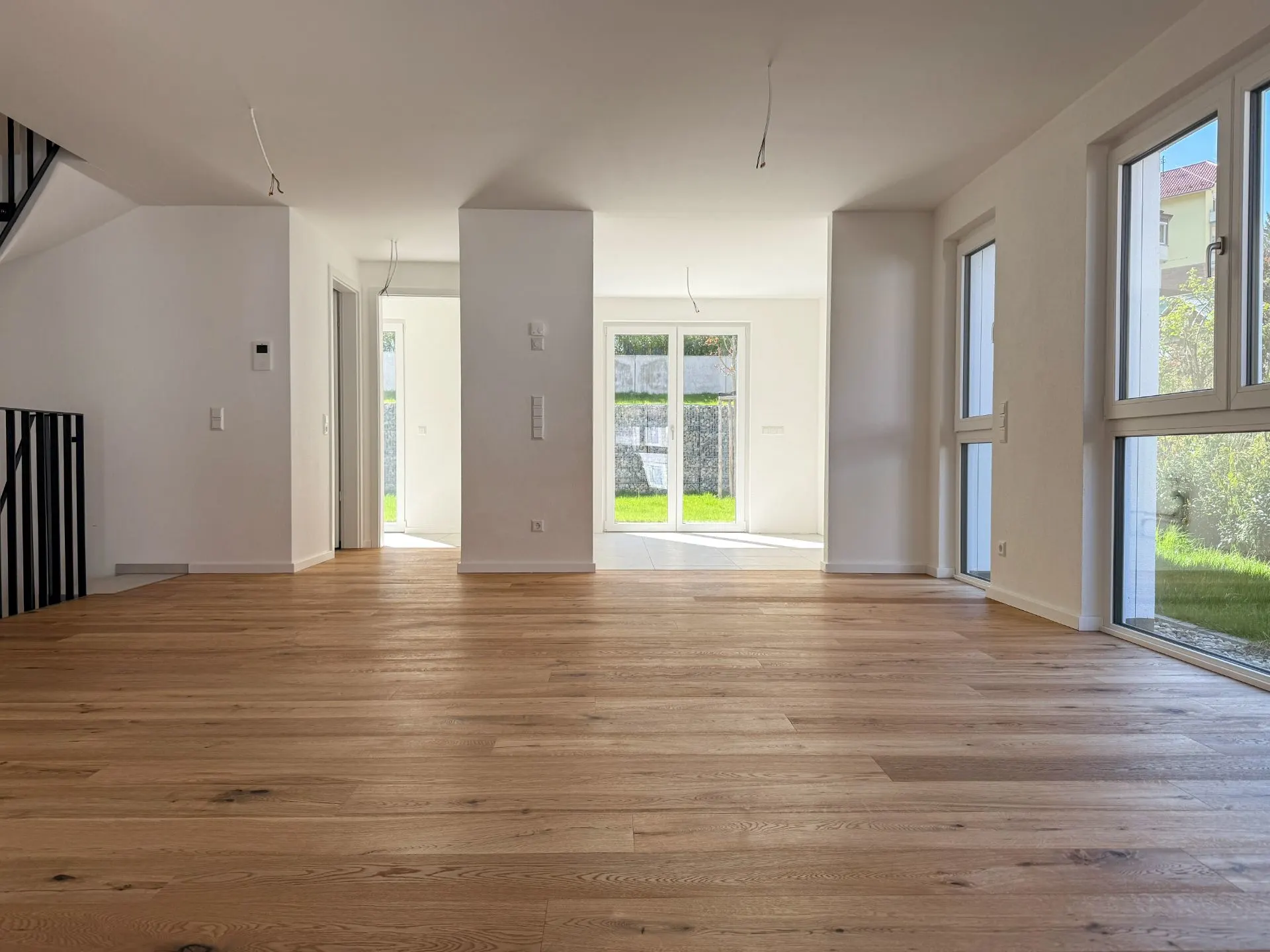 Helles Wohnzimmer mit Holzfußboden, großen Fenstern und Blick auf den Garten.