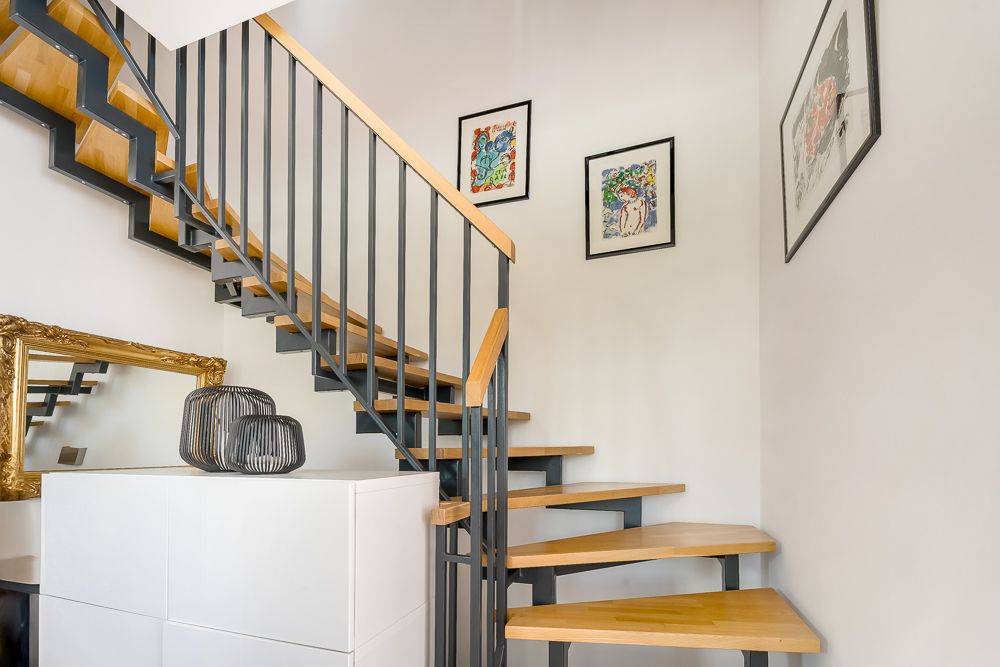 Moderne Holztreppe mit schwarzem Geländer und Bildern an weißen Wänden.