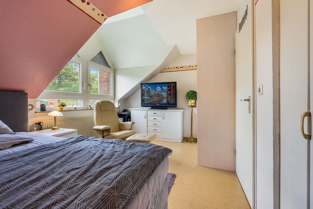 Helles Schlafzimmer mit Doppelbett, Sessel, Fernseher, großen Fenstern und Dachschrägen.