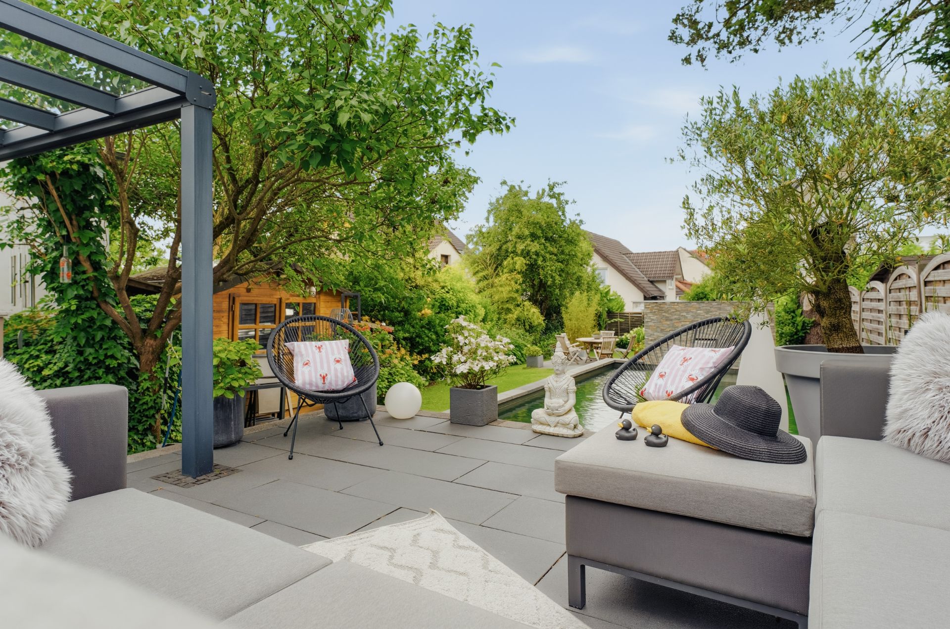 Moderne Terrasse mit Sitzmöbeln, Kissen und Blick auf einen grünen Garten mit Bäumen.