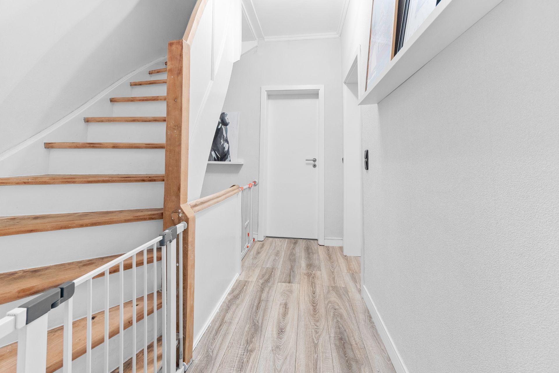 Heller Flur mit Holztreppe, Baby-Schutzgitter und weißer Tür am Ende.