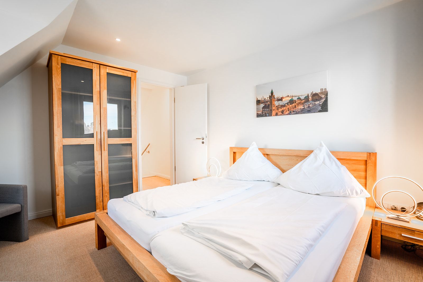 Helles Schlafzimmer mit Holzbett, Kleiderschrank und Bild an der Wand.