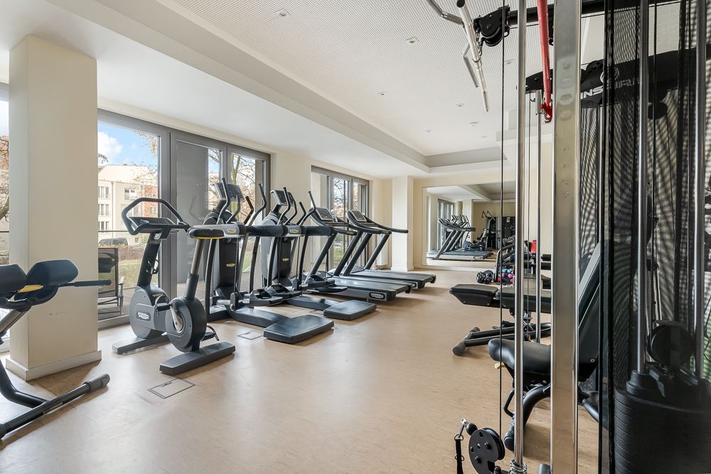 Fitnessraum mit Laufbändern, Crosstrainern und Kraftgeräten, große Fenster an der Seite.