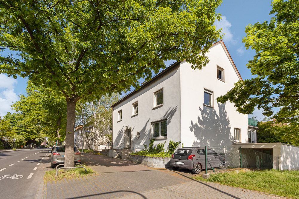 Zweistöckiges Wohnhaus an einer Straße mit geparkten Autos und Bäumen.