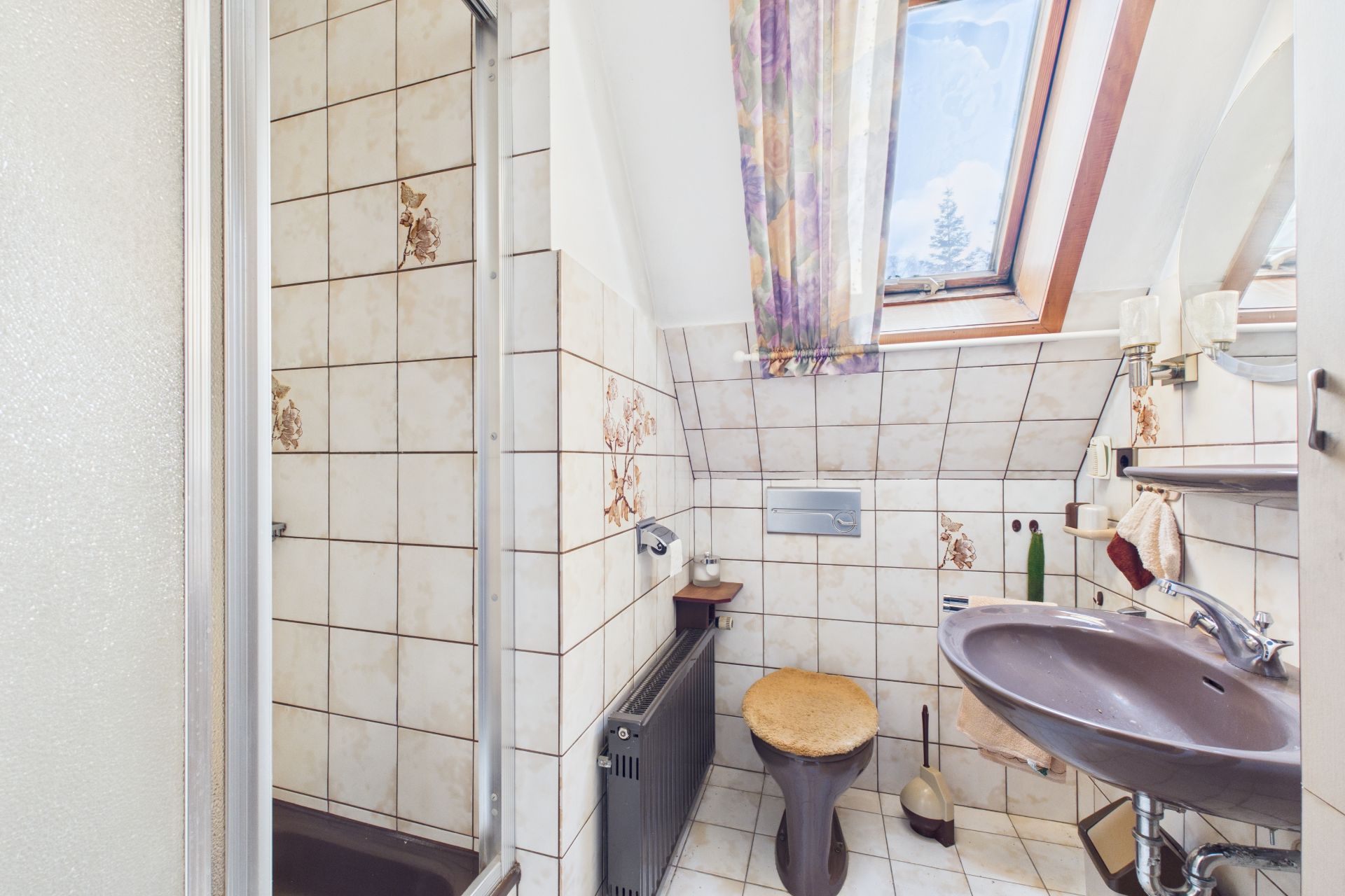 Kleines Badezimmer mit brauner Toilette, Waschbecken, Dusche und Dachfenster.