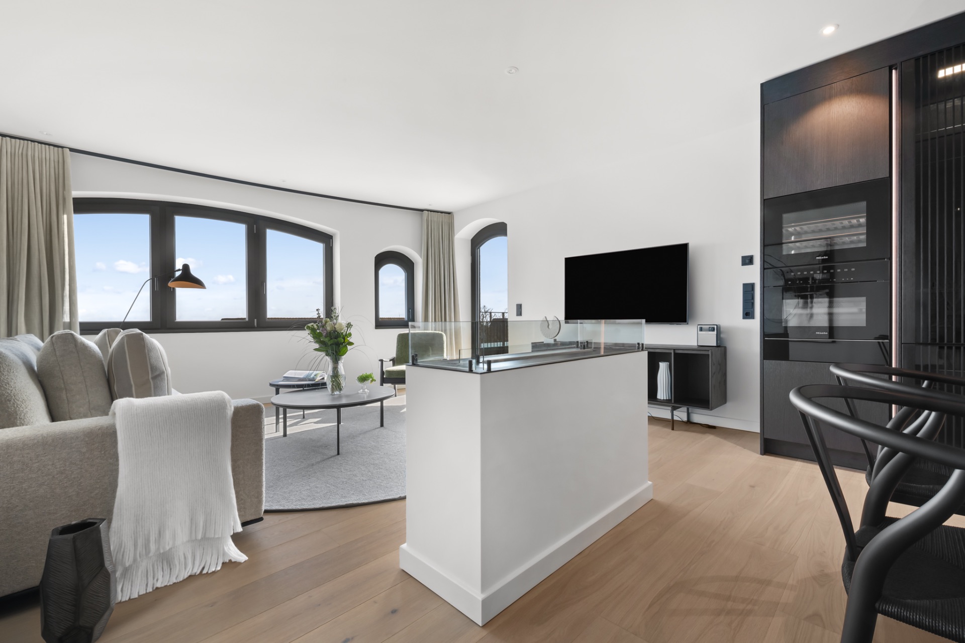 Modernes Wohnzimmer mit Sofa, Couchtisch, TV, großen Fenstern und Holzboden.
