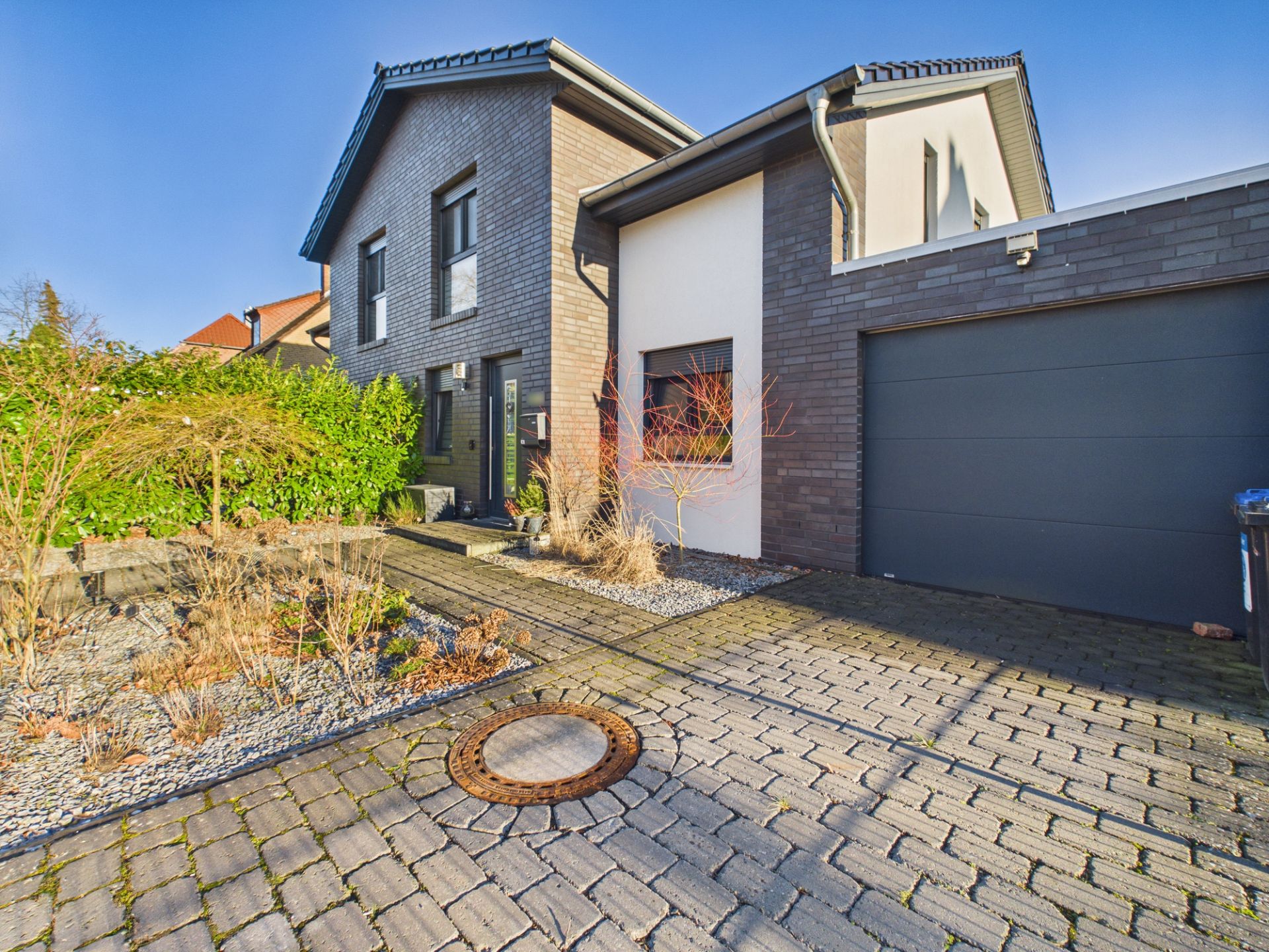 Moderne Doppelhaushälfte mit Einfahrt, Garage und gepflegtem Vorgarten mit Kies und Pflanzen.
