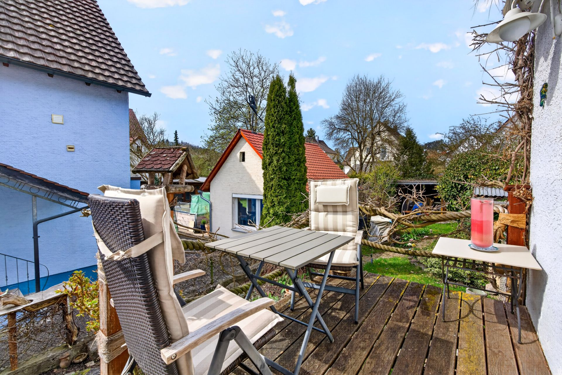 Kleine Terrasse mit zwei Stühlen, Tisch und Kerze, Blick auf Garten und Nachbarhäuser.