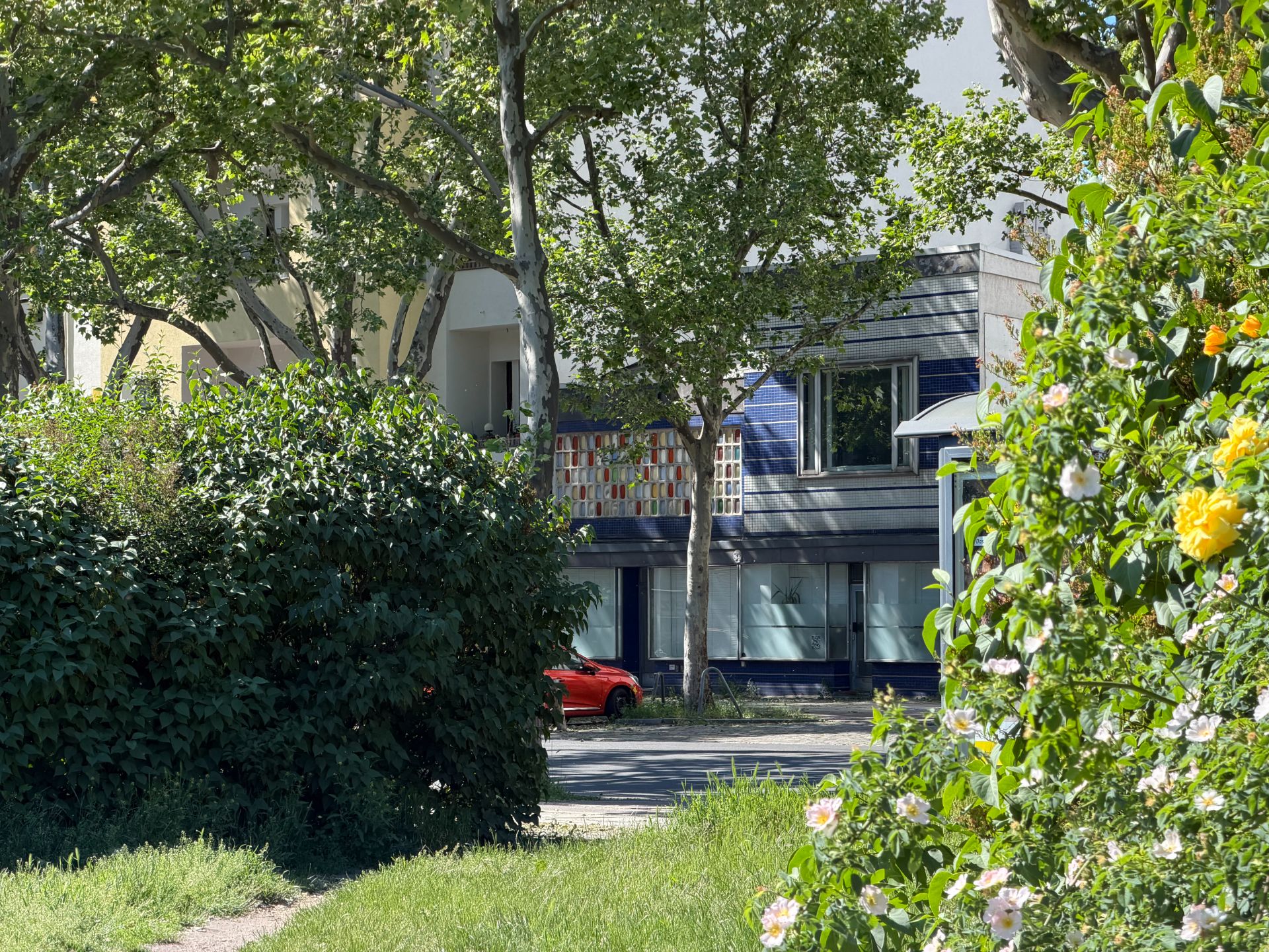 Moderne Wohngebäude hinter Bäumen und grünen Büschen, mit Blumen im Vordergrund.
