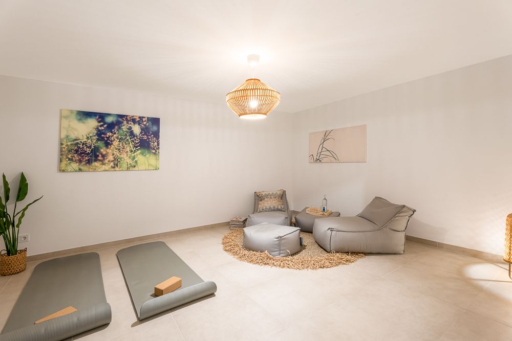 Heller Raum mit zwei Yogamatten, Sitzsäcken, Pflanzen und Wandbildern.