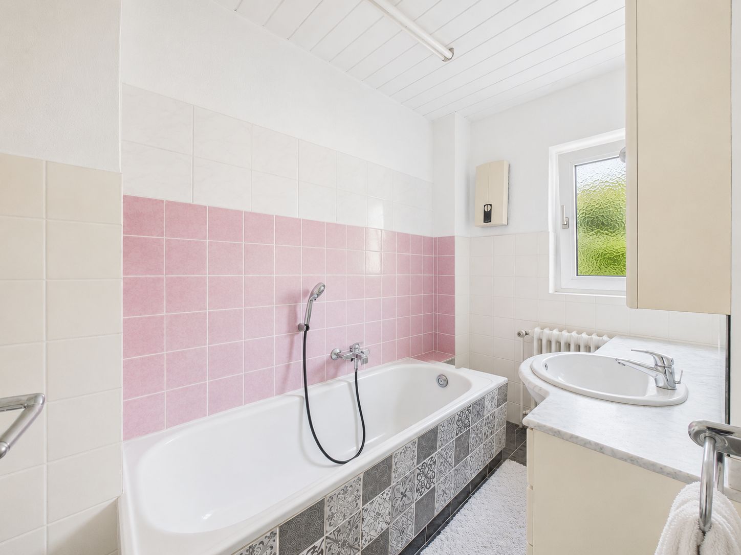 Helles Badezimmer mit Badewanne, rosa Fliesen, Waschbecken und Fenster.