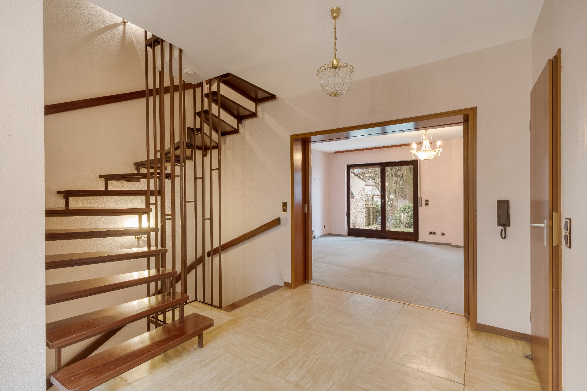 Heller Flur mit Holztreppe und Blick in ein Wohnzimmer mit großen Fenstern.