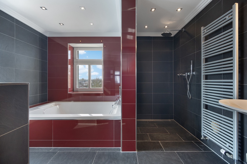 Modernes Badezimmer mit großer Badewanne, Dusche, Handtuchheizkörper und Fenster.