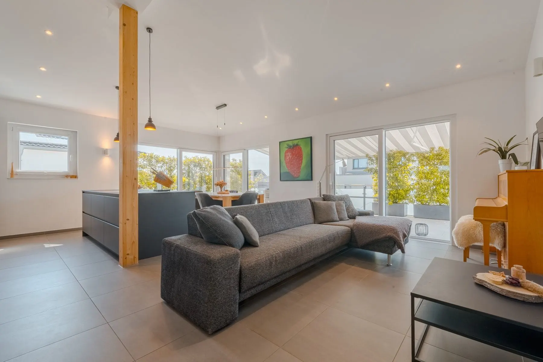 Modernes Wohnzimmer mit grauem Sofa, Klavier, großem Fenster und Zugang zur Terrasse.