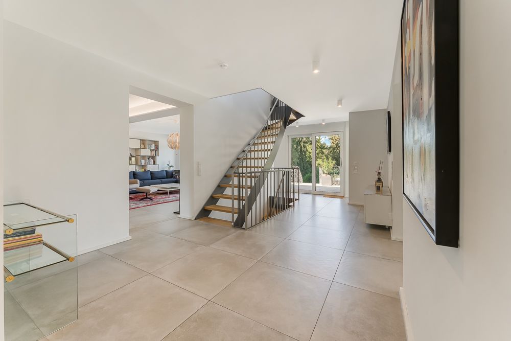 Heller Flur mit offener Treppe, großem Fenster und Zugang zum Wohnzimmer mit Sofa.