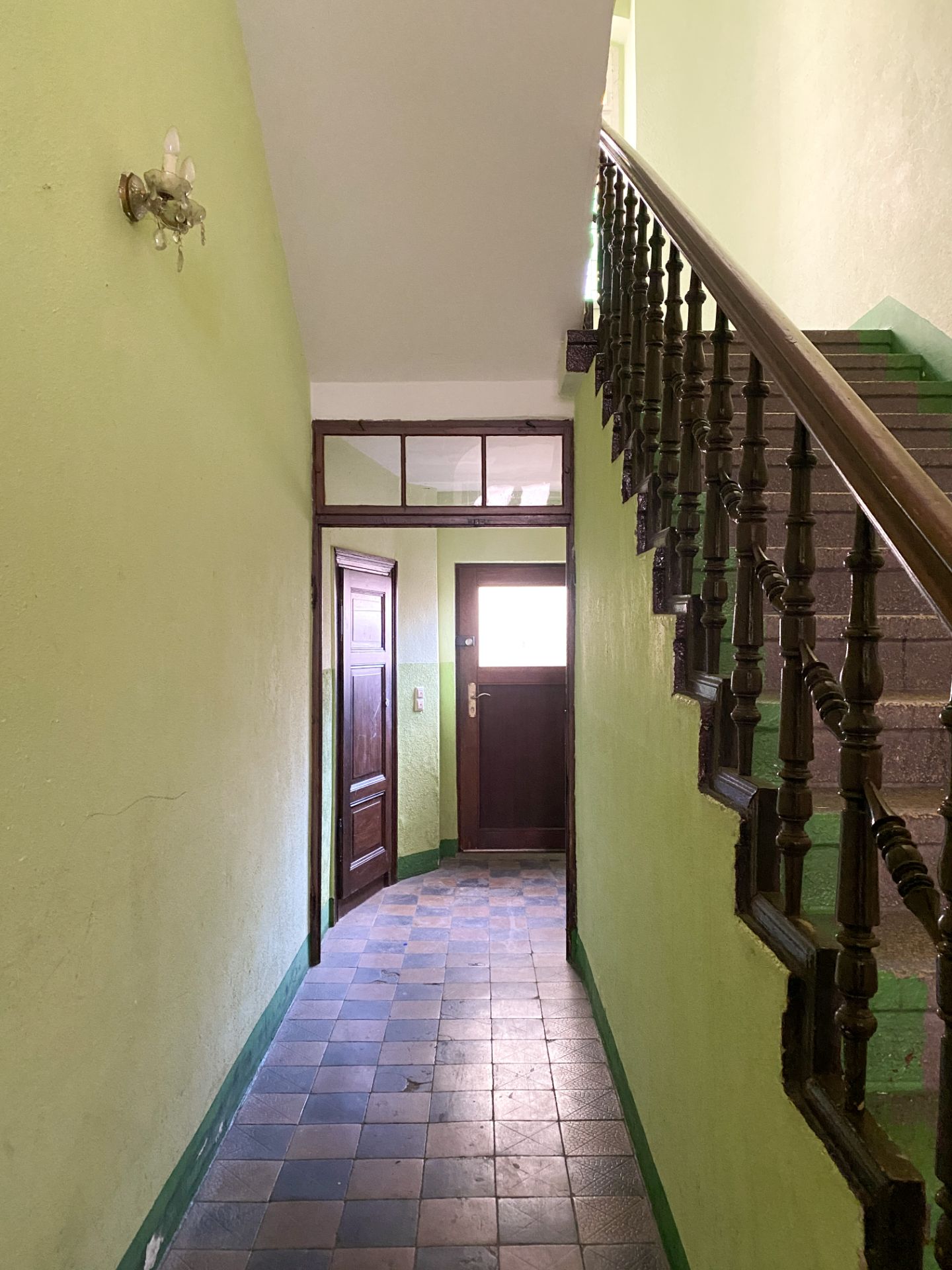 Flur mit grün gestrichenen Wänden, brauner Treppe und Holztür mit Fenster.