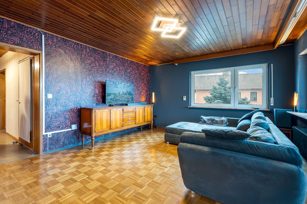 Wohnzimmer mit Holzboden, großer Ecksofa, TV auf Sideboard und Fenster mit Blick nach außen.