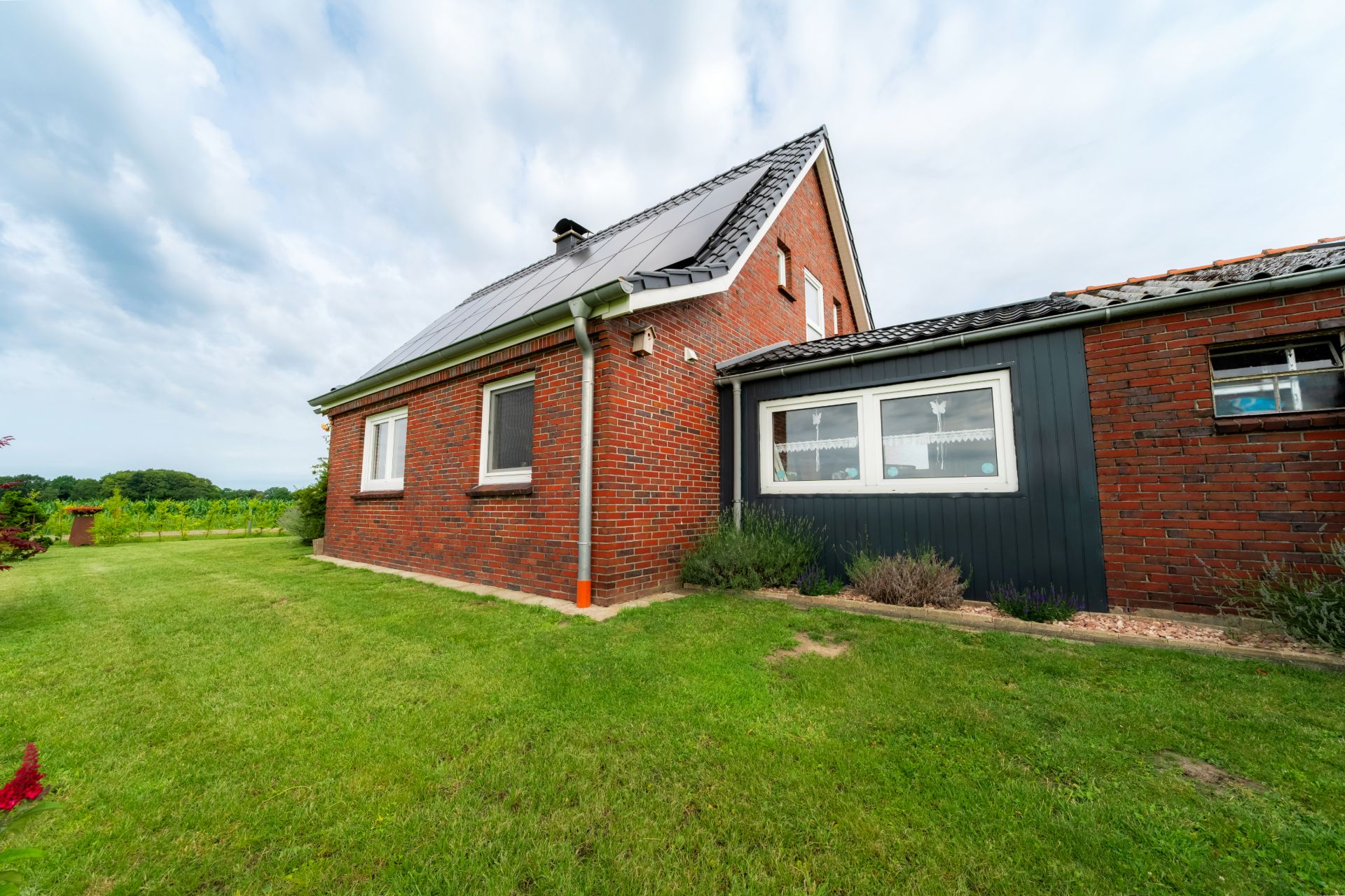 Backsteinwohnhaus mit Solarpanel auf dem Dach und Garten im Vordergrund.