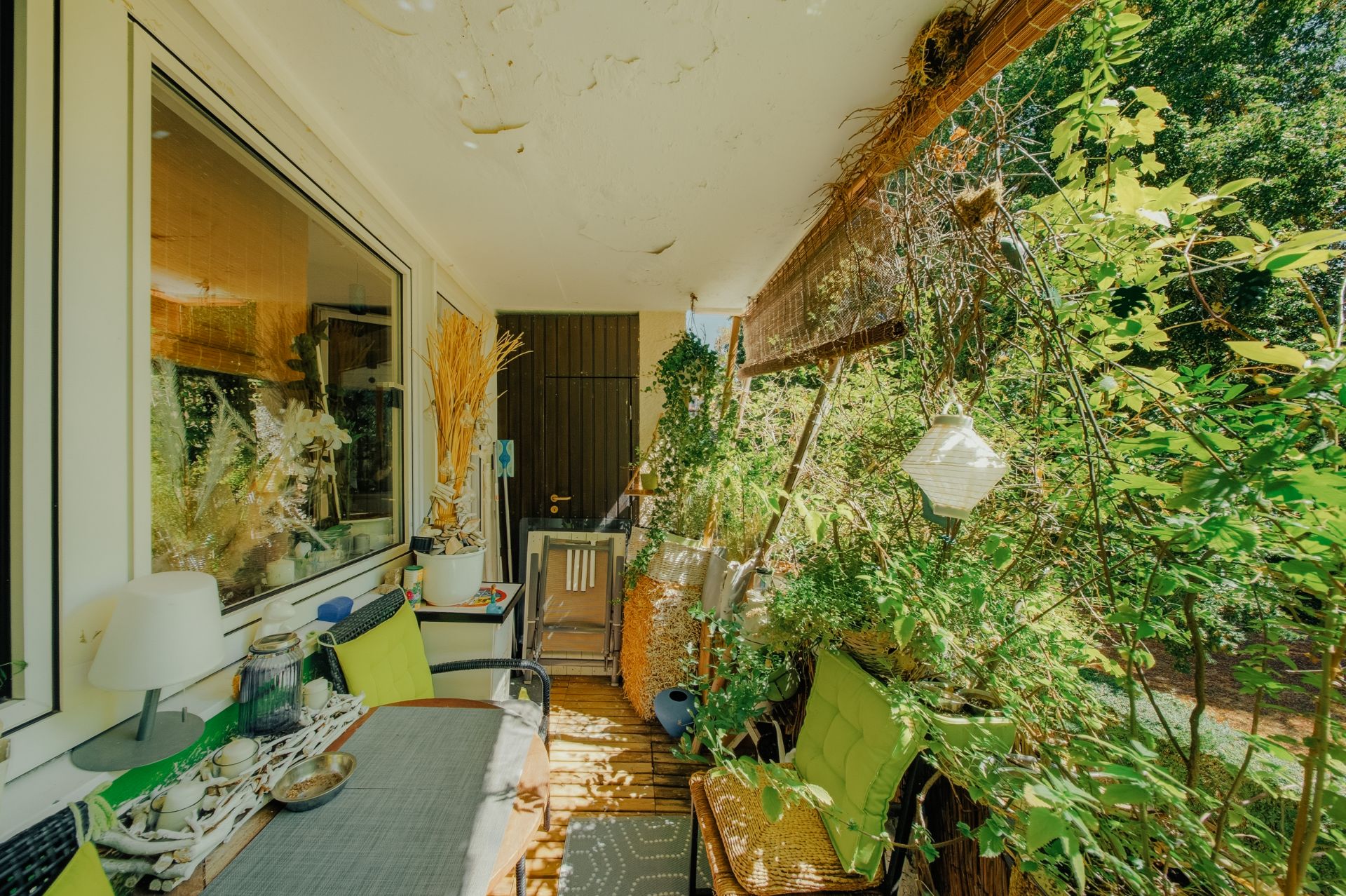 Balkon mit Tisch, Stühlen, Pflanzen und Dekoration, teilweise überdacht und sonnig.