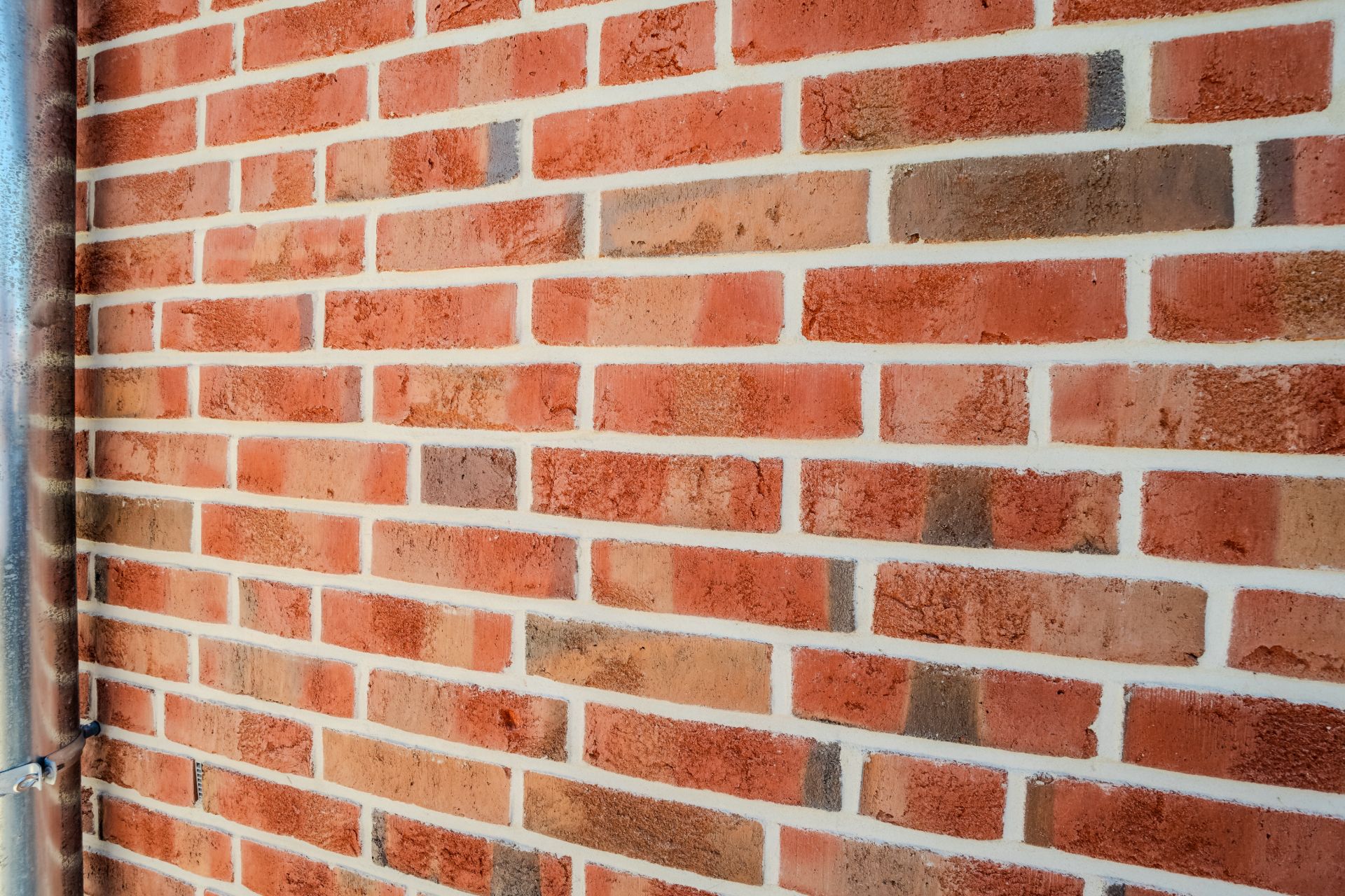 Nahaufnahme einer roten Ziegelsteinwand mit einem Metallrohr an der linken Seite.