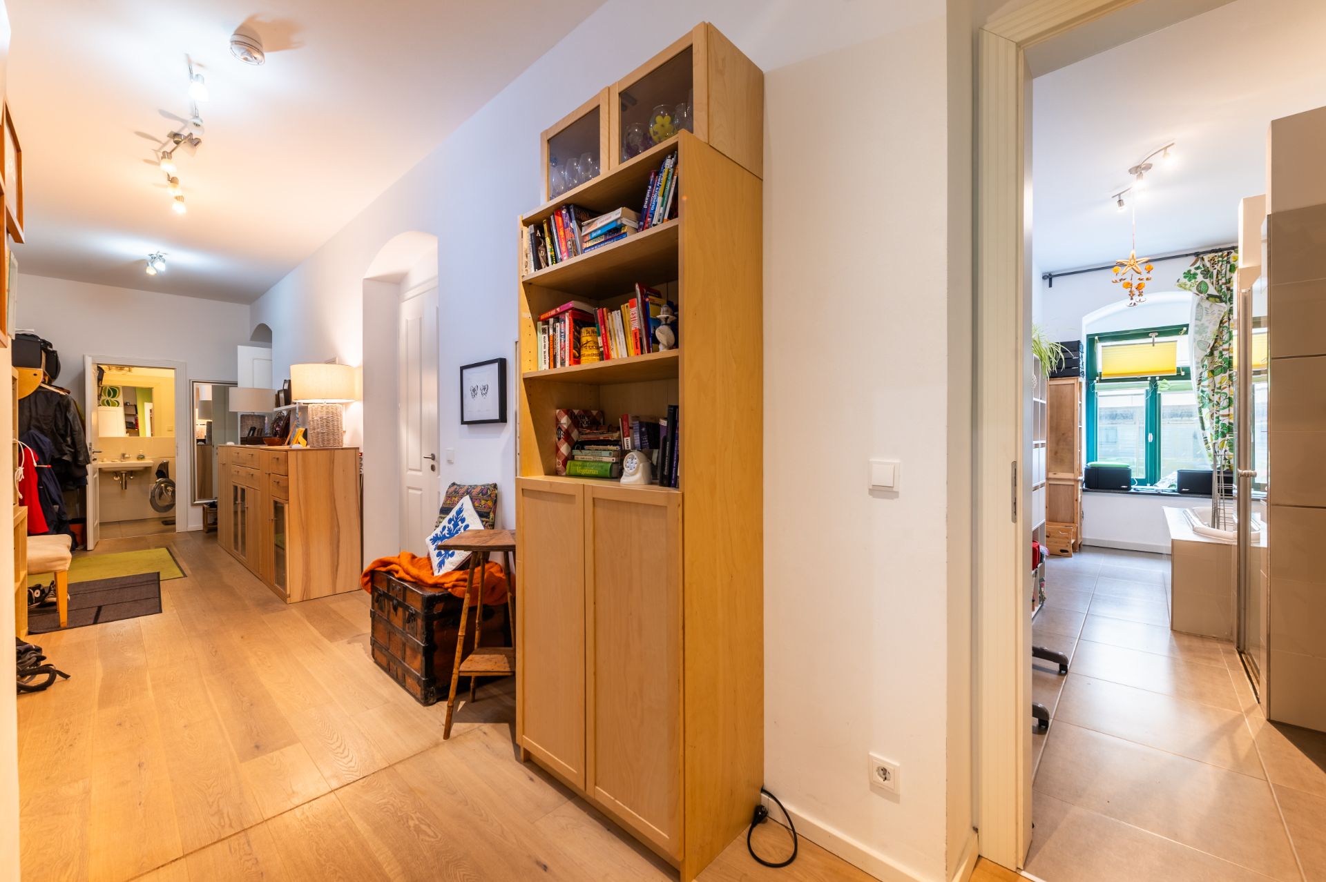 Heller Flur mit Holzregal, Blick in ein Badezimmer und weiteren Wohnraum mit Fenster.