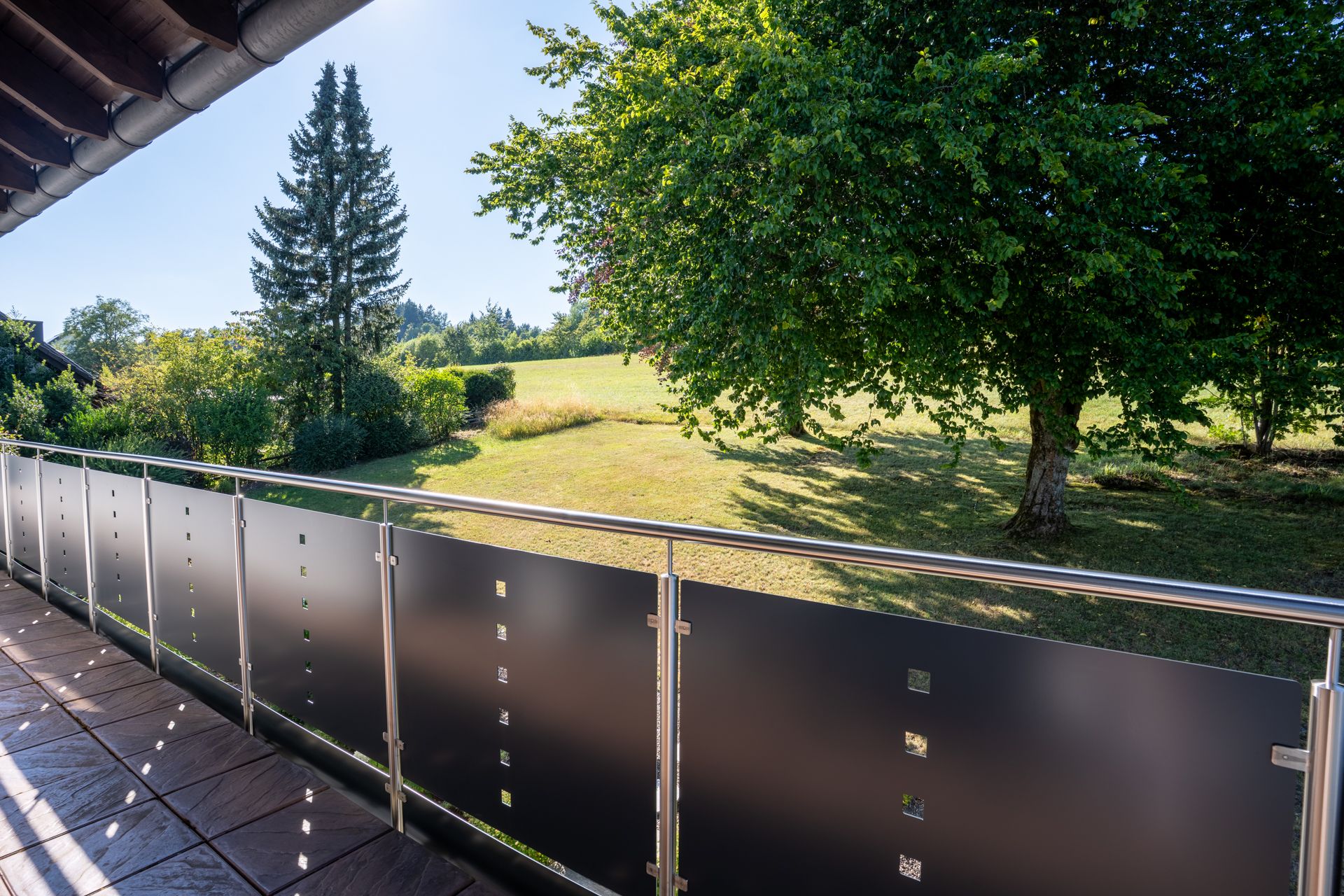 Balkon mit Metallgeländer, Blick auf grünen Garten mit Bäumen und Rasenfläche.