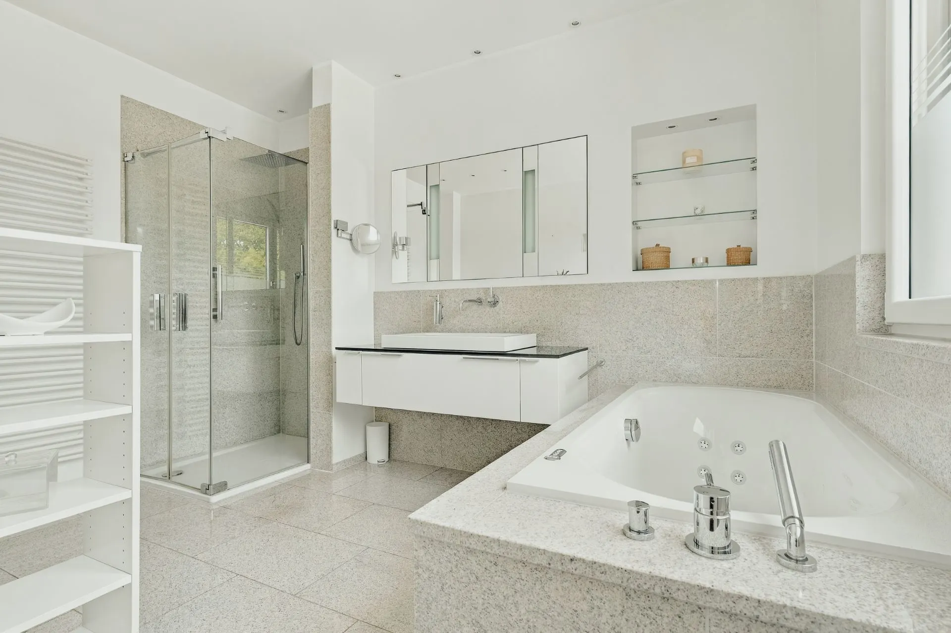 Modernes Badezimmer mit Eckbadewanne, Glasdusche, Waschbecken und weißen Regalen.