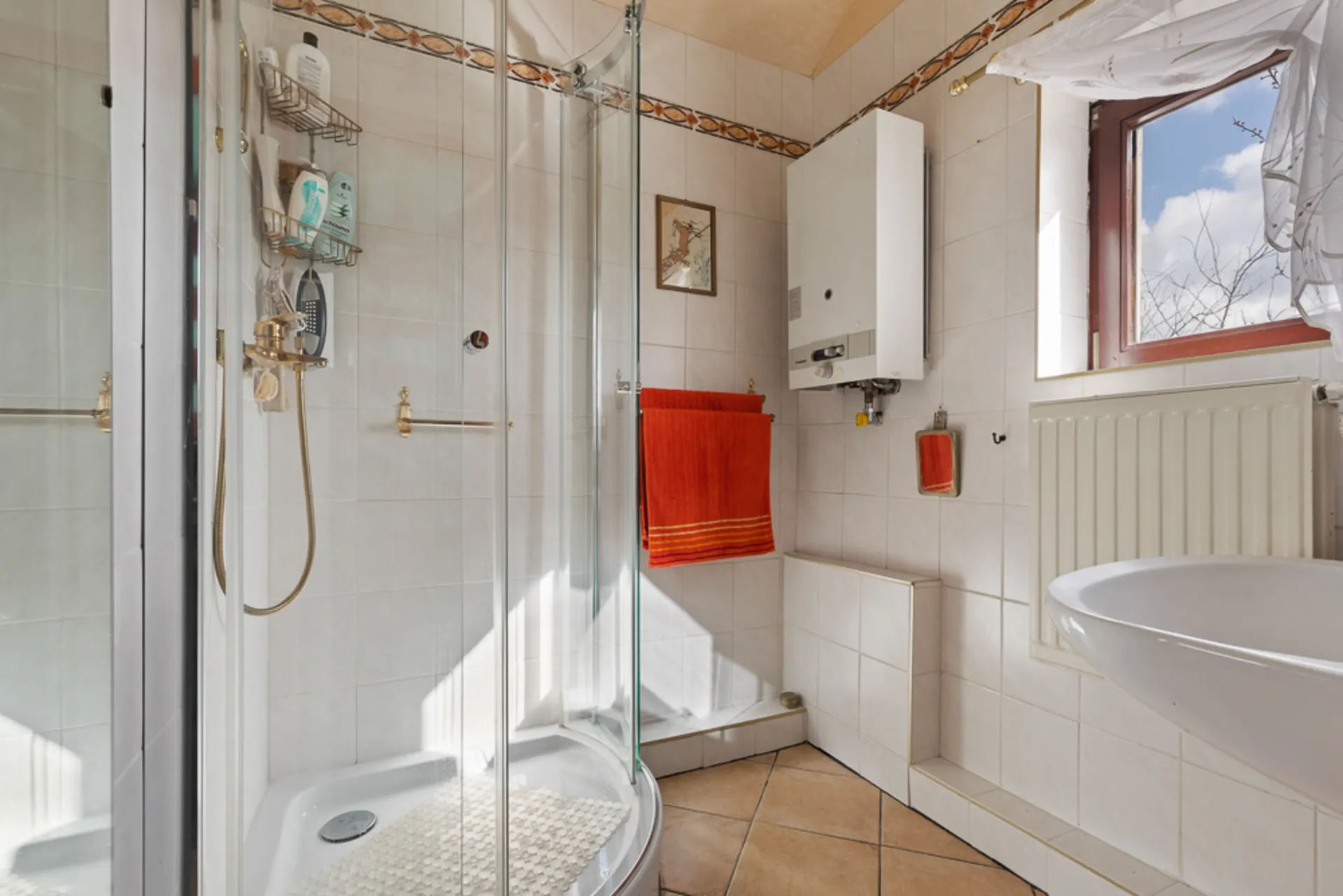 Kleines Badezimmer mit Eckdusche, Waschbecken, Heizung und Fenster mit Vorhang.