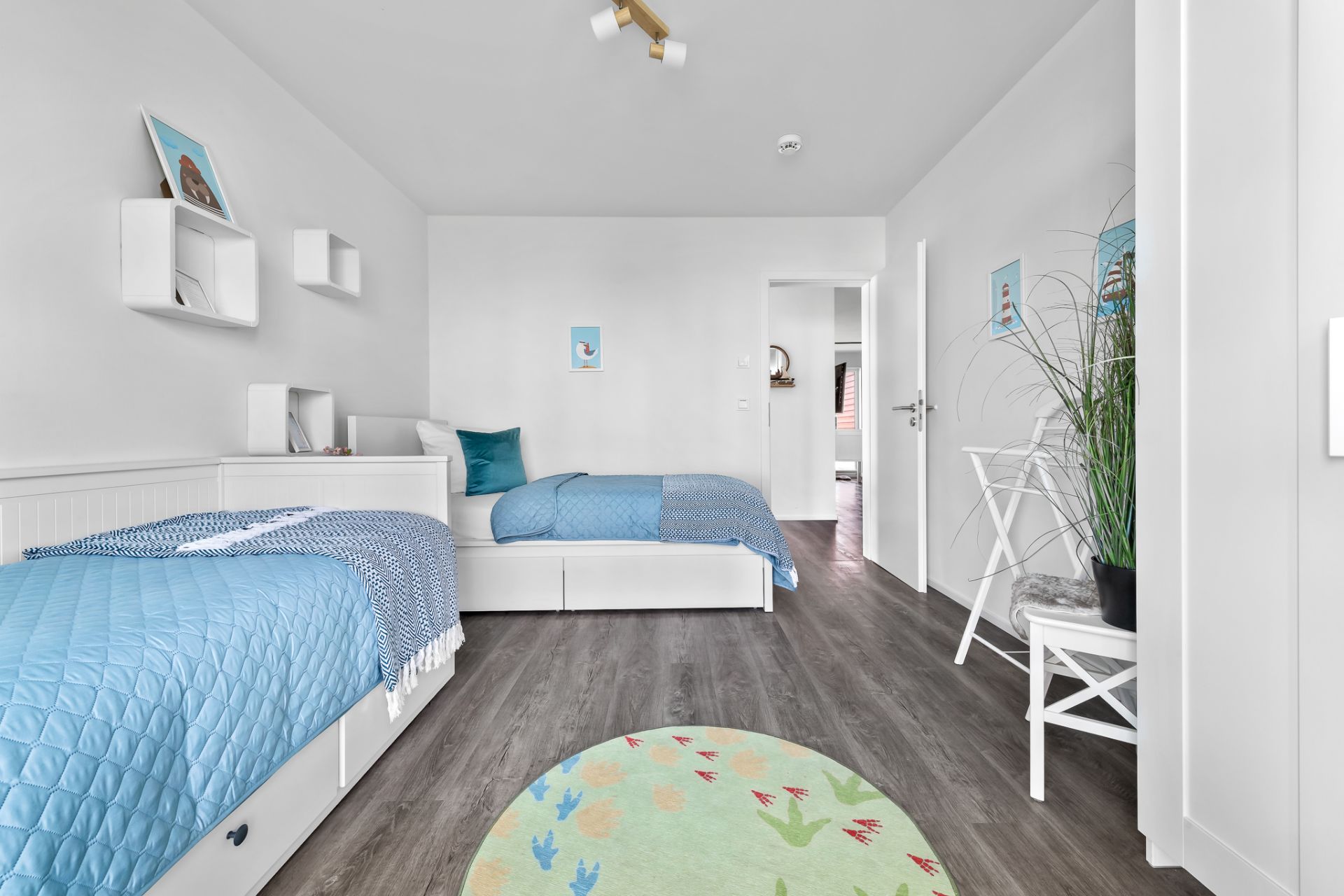 Helles Schlafzimmer mit zwei Einzelbetten, Holzboden, Pflanzen und Wandbildern.