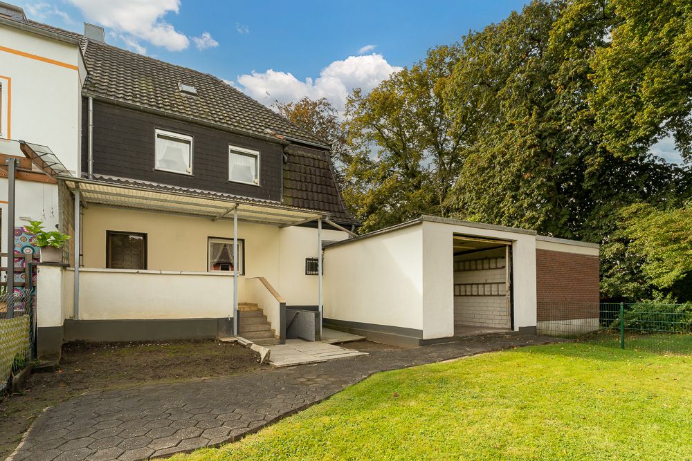 Rückseite eines Wohnhauses mit überdachtem Eingang, Garage und Rasenfläche.