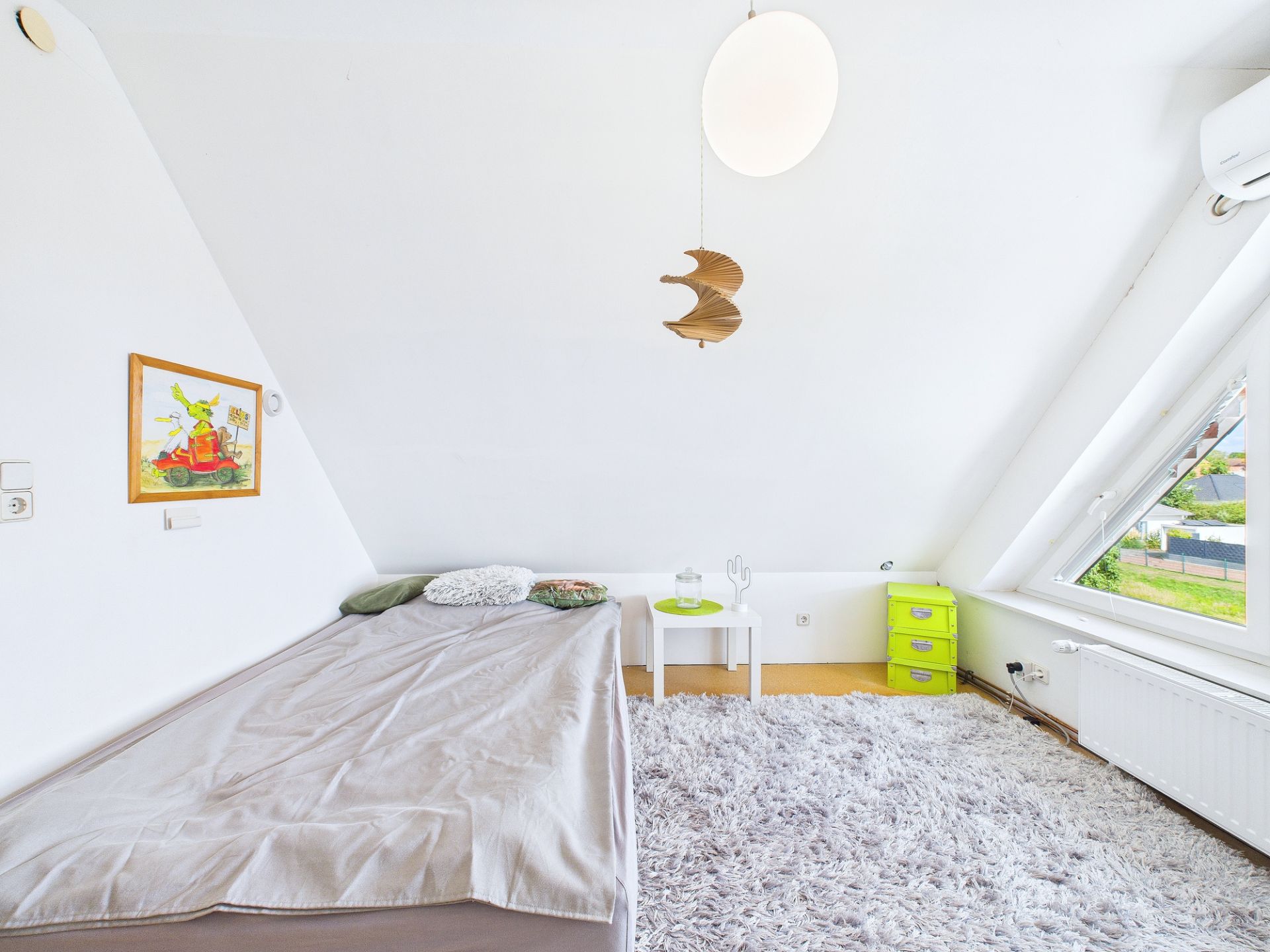 Helles Schlafzimmer mit Einzelbett, weißem Teppich, Nachttisch und schrägem Fenster.