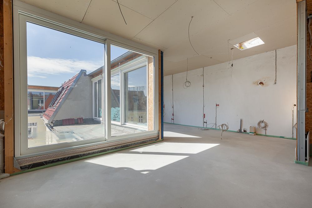 Heller, unfertiger Raum mit großen Fenstern und sichtbaren Kabeln an der Decke.