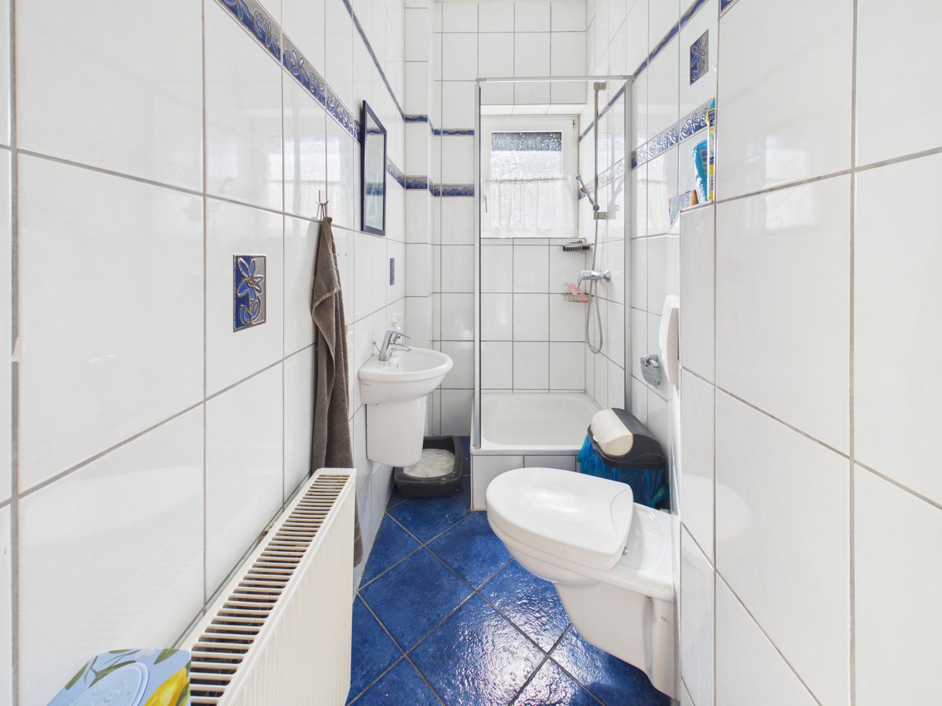 Kleines Badezimmer mit Dusche, WC, Waschbecken und blau-weißen Fliesen.