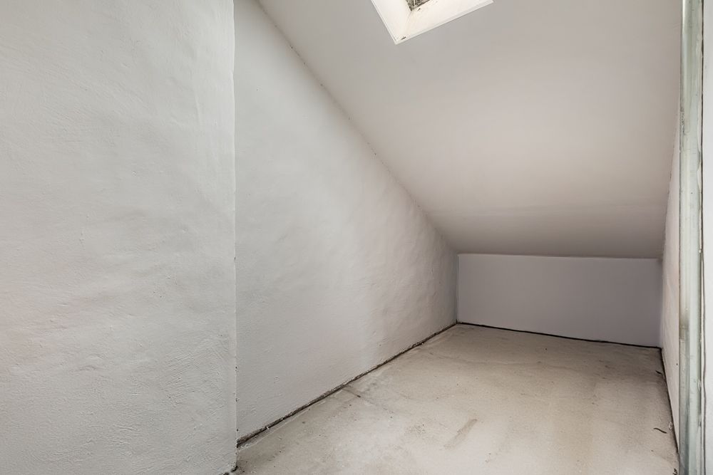 Leerer, weiß gestrichener Raum mit schräger Decke und kleinem Dachfenster.