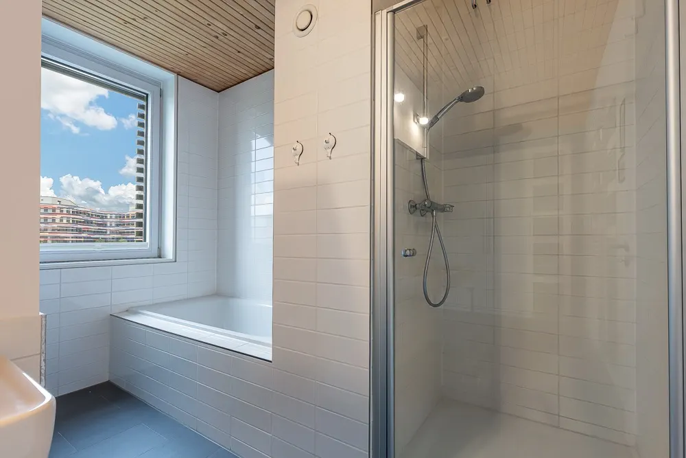 Modernes Badezimmer mit Badewanne, Fenster und verglaster Dusche mit Handbrause.