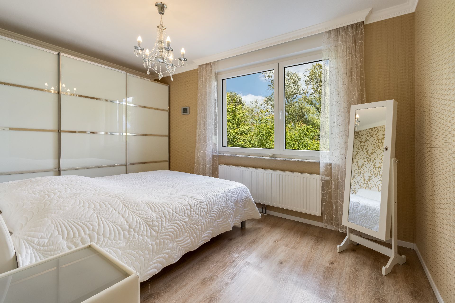 Helles Schlafzimmer mit großem Bett, Spiegelschrank, Fenster und Stehspiegel.