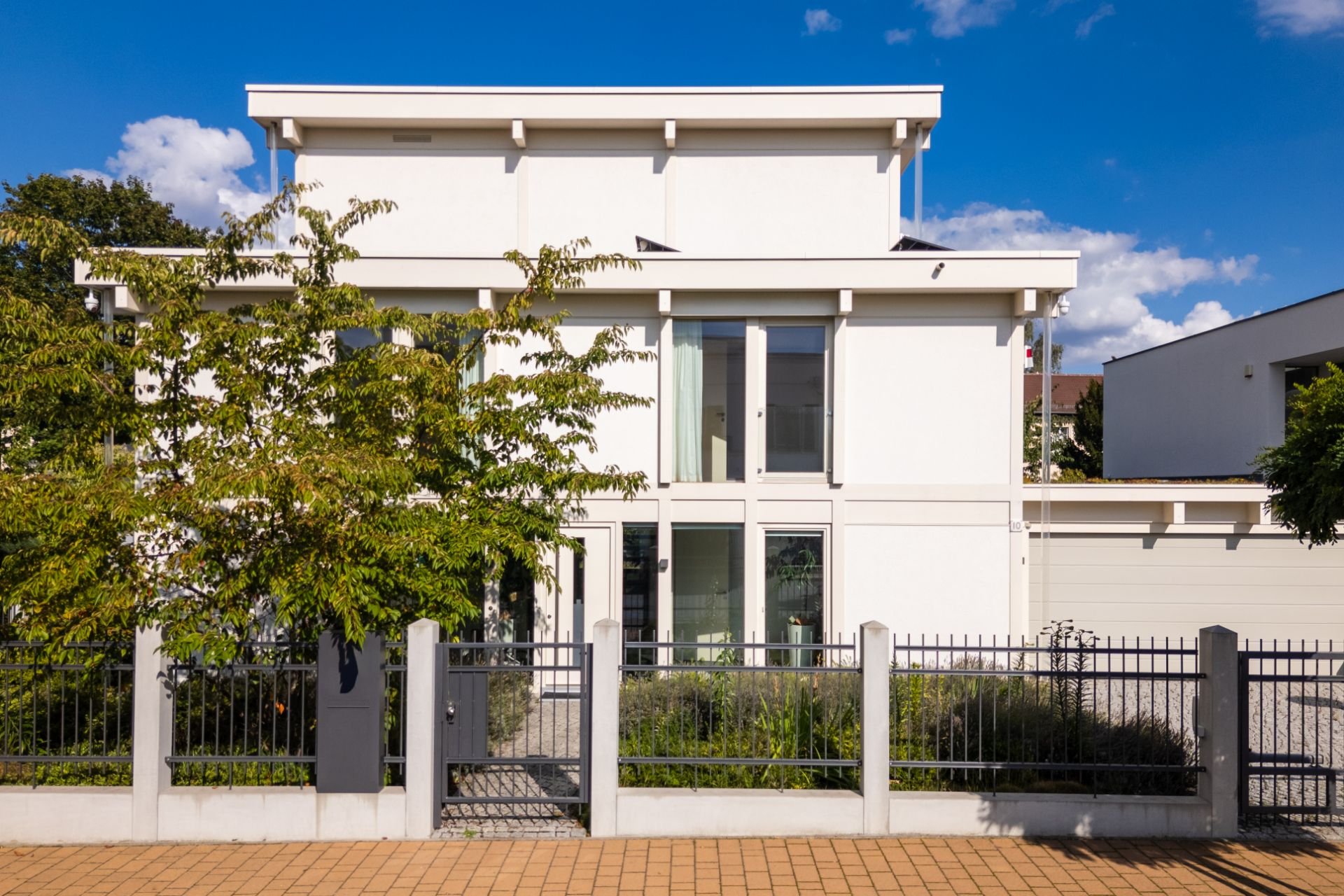 Modernes, weißes Wohnhaus mit großem Fenster, Garten und Zaun im Vordergrund.