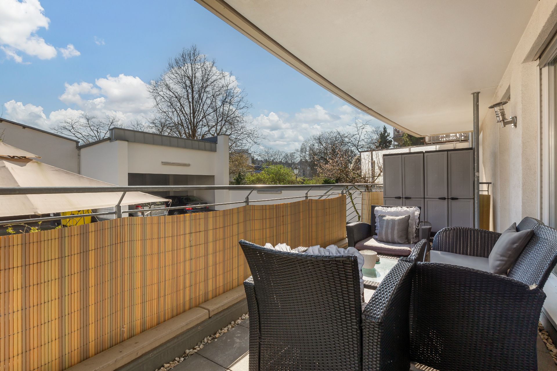 Überdachter Balkon mit Sitzgruppe, Tisch, und Aufbewahrungsschränken, umgeben von Bambusmatten.